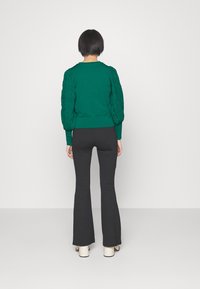Pull vert avec manches bouffantes texturées, assorti à un pantalon noir évasé ajusté et des chaussures plateformes crème. Fini tissu lisse.