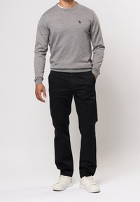 Grå stickad tröja med ribbad krage och muddar, i kombination med svarta byxor. Vita sneakers fulländar outfiten. Undanträngd logotypdetalj på tröjan.