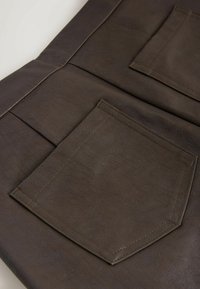 Țesătură din piele ecologică maro, cu două buzunare, având cusături vizibile. Suprafața are o textură moale și un luciu subtil.