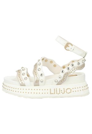 Sandales à plateforme blanches avec clous décoratifs et strass. Caractérisées par une semelle épaisse et une bride de cheville avec boucle. Le nom de la marque est affiché sur le côté.