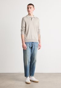 Ljusgrå stickad tröja med krage, kombinerad med blekblå raka jeans och vita sneakers med bruna sulor.