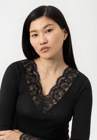 Sort langærmet top med en blomsterløsning i V-udskæring og tekstureret ribbet stof. Spidsblonde detaljer har bølgede kanter og blomster mønstre.