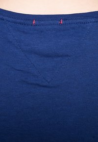 Mörkblått tyg med en slät yta, med en triangulär sömdetalj vid halslinningen i kontrasterande röd tråd.