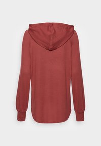 Roter Kapuzenpullover mit strukturiertem Stoff, langen Ärmeln mit schmalen Bündchen und abgerundetem Saum. Die Kapuze sitzt eng am Hals.