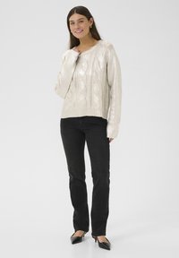 Maglione a maglia cable, di colore argento metallico, con una vestibilità rilassata, maniche lunghe e bordo a costine, abbinato a jeans neri aderenti e décolleté neri a punta.