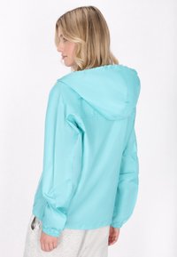 Giacca leggera con cappuccio di un brillante color turchese. Presenta polsini elasticizzati e una texture liscia e lucida. Adatta per abbigliamento casual in diverse condizioni.
