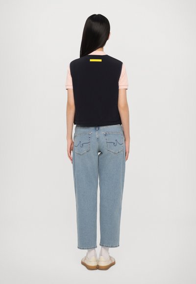 Navy vest with yellow accent over a pink short-sleeve shirt, paired with light blue baggy jeans. White socks and tan slip-on shoes.