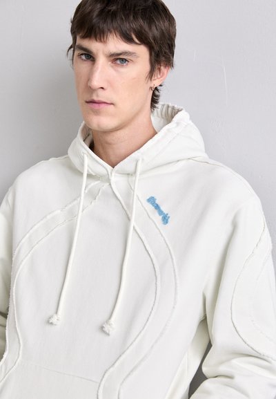 Sudadera blanca con un patrón texturizado y un logo bordado azul en el pecho. Cuenta con cordones gruesos y una suave mezcla de algodón.