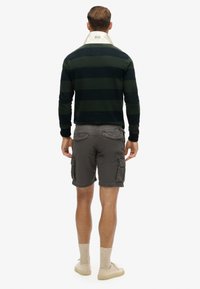 Pull rayé vert foncé et marine avec un col blanc, associé à un short cargo gris et des chaussures beiges. Tissu texturé et poches visibles.