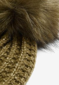 Hnědý pletený čepice s velkým, načechraným kožíškovým pom-pomem. Textura je měkká s proplétaným vzorem a jemnými akcenty nitě.