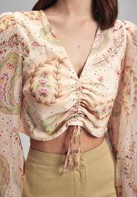 Blumenmuster-bluse in sanften Pastellfarben, mit gerafften Details an der Vorderseite und puffigen langen Ärmeln. Glattes, leichtes Material.