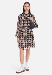 Kleid mit Blumenmuster, langen, schwingenden Ärmeln, tailliertem Schnitt und transparentem Stoff. Kombiniert mit weißen Turnschuhen und Socken.