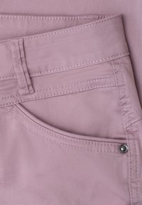 Nahaufnahme einer hellvioletten Hosentasche mit Steppnähten, Gürtelöse und Metallniete auf glattem Stoff.