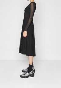 Černé midi šaty s žebrovanými dlouhými rukávy, s plisovanou sukní. V kombinaci se třpytivými stříbrnými platformovými botami a černými kotníkovými ponožkami.