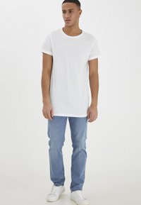 Camiseta blanca de cuello redondo con mangas cortas enrolladas, combinada con jeans azul claro y zapatillas blancas. Diseño simple y casual sin patrones.
