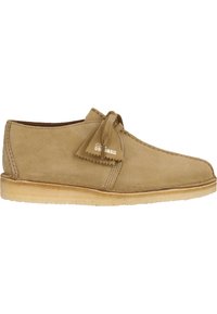 Beige mokkasini kengät, joissa on pyöreä terä, nauhakiinnitys ja tupsu yksityiskohtana. Varustettu kevyellä vaaleanruskealla kumipohjalla, jossa on ommellut reunat kestävyyden lisäämiseksi.