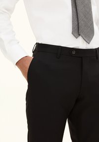 Schwarze, taillierte Hose mit glatter Textur, ausgestattet mit einem Knopfverschluss und Seitentaschen. Kombiniert mit einem weißen Hemd und einer grauen Krawatte.