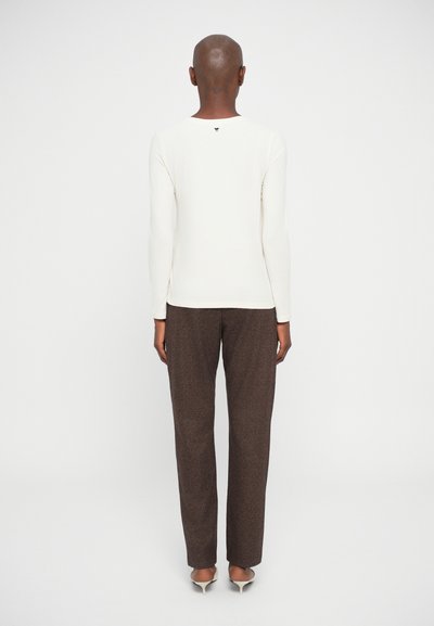 Ivoor blouse met lange mouwen en bruine patronen broek, achterkant zichtbaar, met een ronde halslijn en subtiel logo-detail bij de hals.
