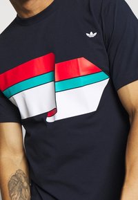 Marinfärgad t-shirt med en stor grafik i röd, teal och vit. Tillverkad av bomull med rund halsringning och en liten vit logotyp på bröstet.