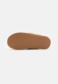 Semelle en caoutchouc marron avec surface texturée et logo en relief. Tige rembourrée, recouverte de fourrure crème, offrant un design doux et durable.