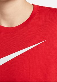 Läheltä otettu kuva kaulasta ja ylärinnasta, päällä punainen pyöreäkauluksinen t-paita, jossa on suuri valkoinen Nike-swoosh-logo.