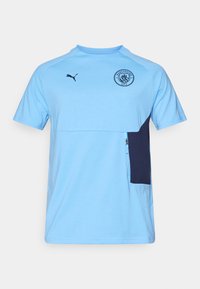 Lys blå kortærmet t-shirt med en marineblå lomme, med rund halsudskæring, Puma-logo og Manchester City-emblem på brystet.