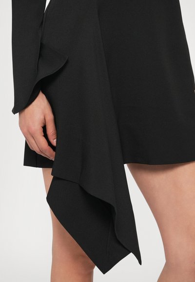 Čierne šaty s asymetrickým lemom, vyrobené z hladkej tkaniny. Majú volánikový detail na rukáve a záhybovú textúru v oblasti pása.