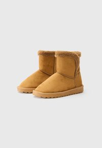 Une paire de bottes d'hiver en suede beige mi-hautes avec une doublure en fourrure moelleuse et des semelles en caoutchouc sur un fond gris clair.