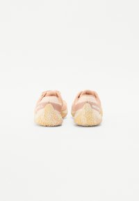 Zapatillas deportivas de color rosa claro con parte superior de malla texturizada y suela de goma, que presentan un patrón zigzagueante distintivo y un talón reforzado.