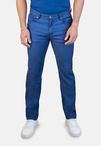 Jeans de hombre en denim azul con un corte recto, cinco bolsillos y detalles en botón de cobre, combinados con zapatillas blancas. Textura suave y lavado medio.