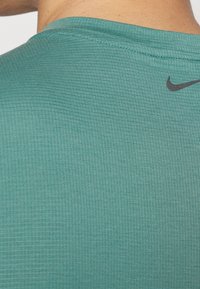 Turkoosi urheilupaita, jossa on teksturoitu, ribatty kangas. Musta Nike-logo sijoitettu yläselkään. Yksinkertainen, pyöreä kaula-aukkosuunnittelu.