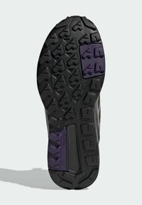 Semelle de chaussure en caoutchouc noir et violet avec des crampons profonds, triangulaires et rectangulaires irréguliers pour une meilleure traction.