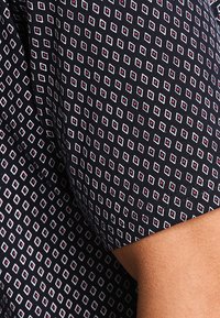 Tela negra con un patrón geométrico de diamantes en blanco y rosa. Mangas cortas y textura suave con detalles de costura visibles.