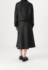 Musta tweed-takki ja hame-setti, jossa on tekstuurinen kangas metallilangalla, lyhyt muotoilu ja levenevä hame-siluetti.