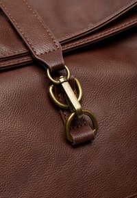 Brown leather bag featuring a textured surface, a flap closure, and a gold-toned metal hardware accent with a dual loop design.