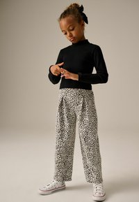 Top negro de manga larga acanalado combinado con pantalones blancos holgados que presentan un patrón de lunares negros, finalizado con zapatillas blancas.