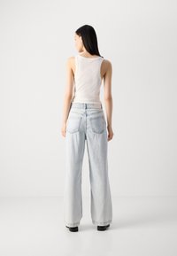 Jean en denim bleu clair à jambes larges, taille haute avec deux poches arrière. Associé à un débardeur ajusté blanc.