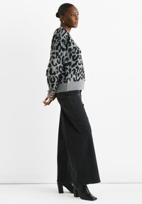 Grauer und schwarzer Leopardenmuster-Pullover mit V-Ausschnitt und oversized Schnitt, kombiniert mit hochtaillierten schwarzen Jeans und schwarzen Absatzstiefeln.