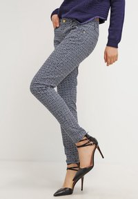 Jeans ajustados de patrón azul con un diseño floral, con un ajuste elegante y acentos de botón dorado, combinados con zapatos de tacón alto negros.