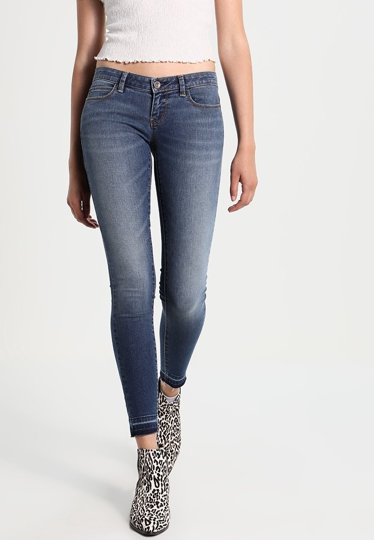 Jeans ajustados de color azul oscuro con un lavado desgastado, que cuentan con bolsillos en la parte delantera y un cierre de botón. Combinados con botas de tobillo con diseño.