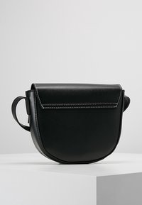 Borsa a tracolla in pelle nera con forma arrotondata, chiusura a dischetto piatta e cuciture bianche a contrasto. Manico laterale per un facile trasporto.