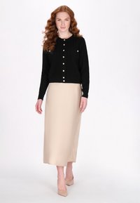 Cardigan nero a maglia con collo rotondo e dettagli a bottoni perlati, abbinato a una gonna midi beige e tacchi nudi. Tessuto dalla consistenza morbida.