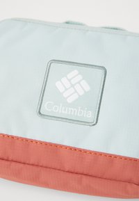 Helles blaues Stofftasche mit strukturiertem Finish, kontrastierendem Korallenboden und dem Columbia-Logo in Weiß auf einem quadratischen Patch gestickt.