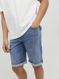 Ljusblå denimshorts med uppvikta fållar och sydda detaljer, tillsammans med en löst sittande vit t-shirt. Slät textur.