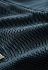 Tissu texturé bleu foncé avec un motif en diamant. Le matériau semble respirant et léger, avec un accent métallique sur un bord.