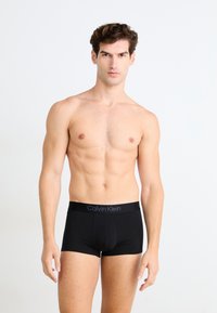 Boxer-briefs noirs pour hommes avec une ceinture en logo Calvin Klein, présentant un design ajusté et une texture de tissu lisse. Le modèle montre une vue de face.