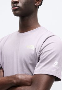 Ανοιχτό μοβ κοντομάνικη μπλούζα από βαμβάκι, με κίτρινο λογότυπο στο στήθος και λευκό λογότυπο στο μανίκι. Κλασικός σχεδιασμός με στρογγυλή λαιμόκοψη.