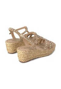 Beige wedge sandalen met een geweven jute zool, voorzien van decoratieve doorzichtige rhinestones en gekruiste banden. Zachte, suede-achtige textuur.