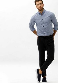 Camicia azzurra chiara a maniche lunghe, pantaloni neri e scarpe blu navy. La camicia presenta una tasca sul petto; i pantaloni hanno un design slim fit.
