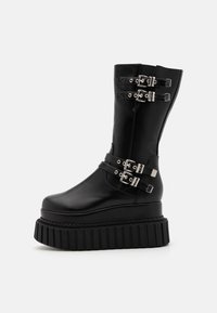 Black platform boots made of smooth faux leather, featuring multiple silver buckle accents and a ribbed sole for added grip.